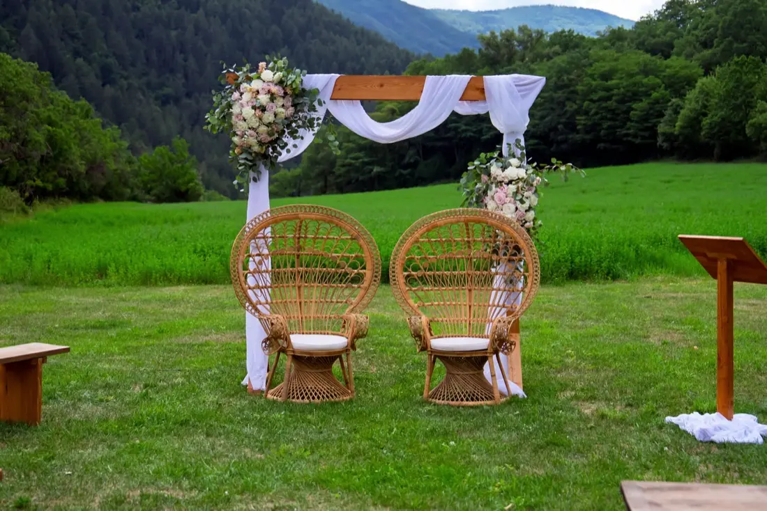 Arche de cérémonie drapée et fauteuils en rotin face aux montagnes