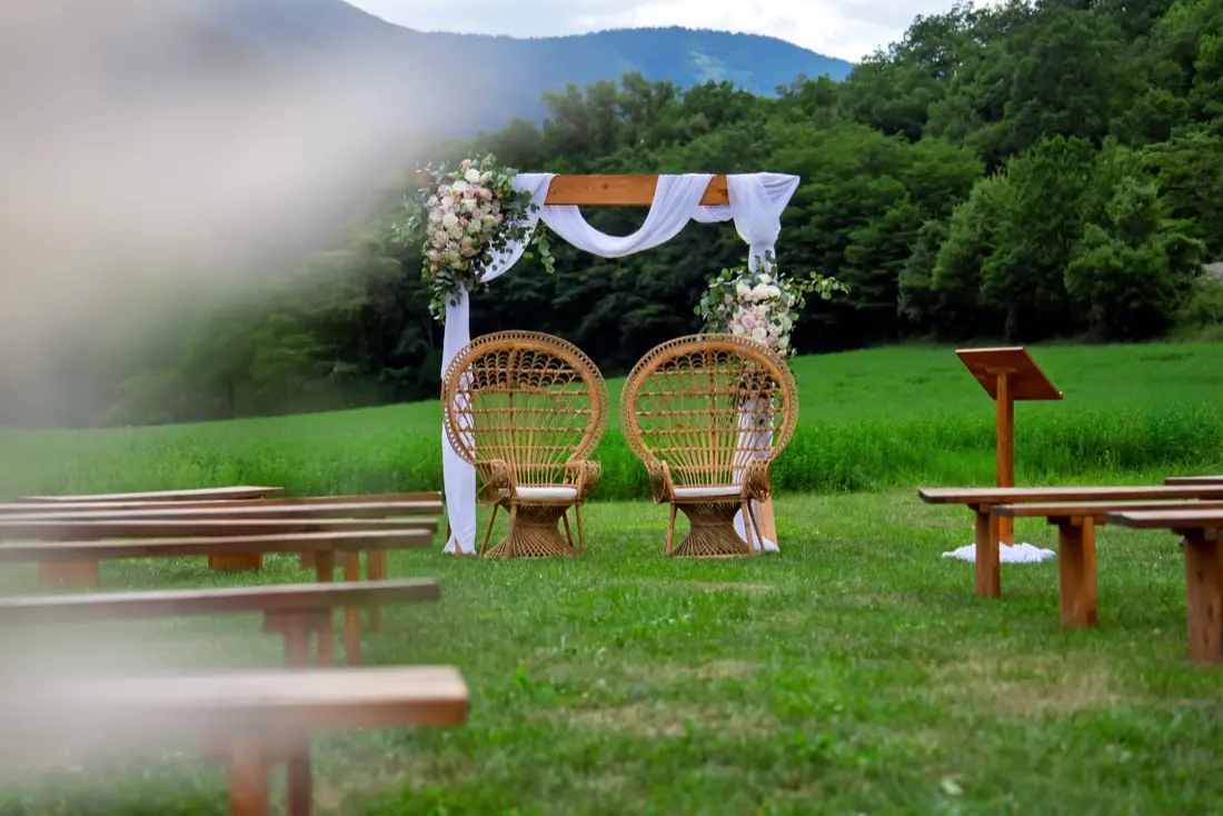 Cérémonie de mariage en plein air, bancs de bois et arche fleurie face aux montagnes