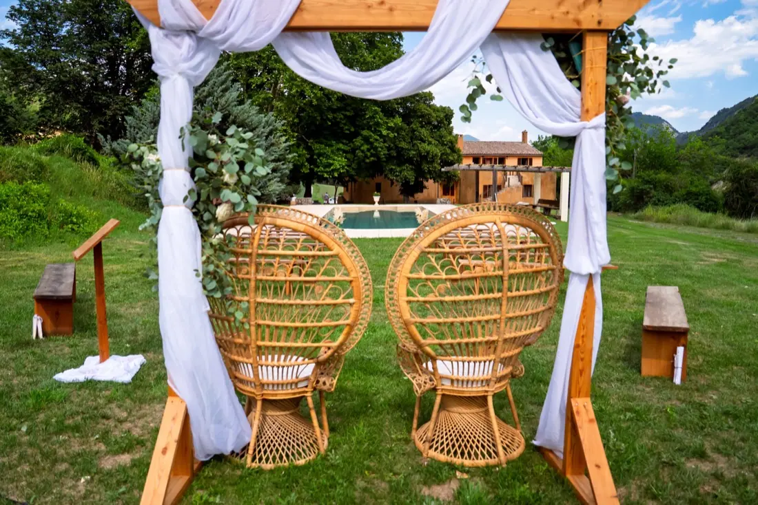 Fauteuils des mariés sous l'arche, face au mas et à la piscine du domaine